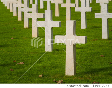 Graves with white crosses arranged in rows on green grass in a memorial cemetery during daylight hours Graves with white crosses arranged in rows on green grass in a memorial cemetery during daylight hours 139417254