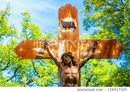Rusty cross with figure of Jesus in a green area under blue sky during daytime Rusty cross with figure of Jesus in a green area under blue sky during daytime 139417305