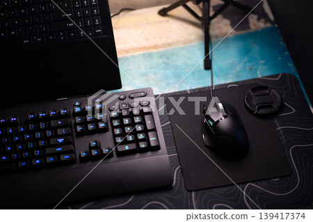 Modern dark gaming keyboard and mouse setup with laptop on desk, illuminated for computing Modern dark gaming keyboard and mouse setup with laptop on desk, illuminated for computing 139417374