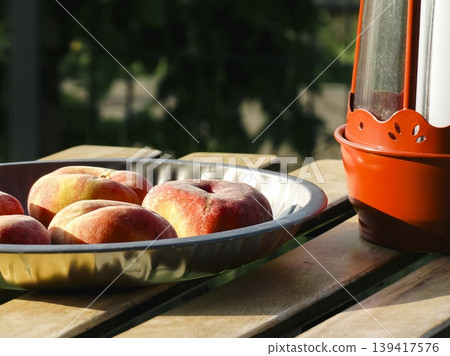 Flat peaches in a metal bowl and red lantern on a wooden table, evoking summer harvest vibes and natural organic fruit aesthetics. Flat peaches in a metal bowl and red lantern on a wooden table, evoking summer harvest vibes and natural organic fruit aesthetics. 139417576