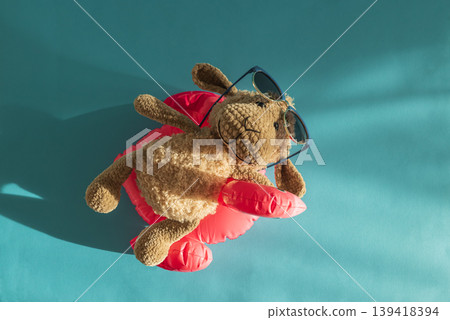 Knitted Plush Sheep in Sunglasses on Pink Pool Flamingo Float Against Blue Water. Knitted Plush Sheep in Sunglasses on Pink Pool Flamingo Float Against Blue Water. 139418394