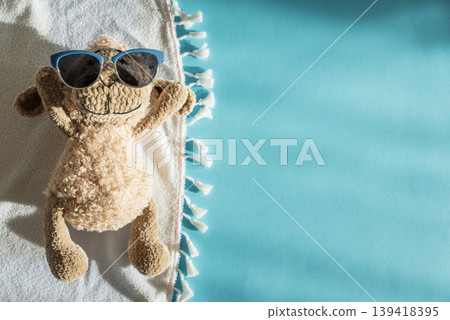 Knitted Plush Sheep Sunbathing on White Towel with Blue Sunglasses Knitted Plush Sheep Sunbathing on White Towel with Blue Sunglasses 139418395