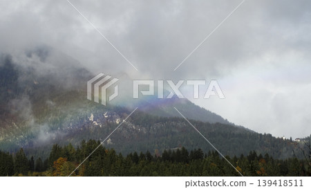 Rainbow arc over a foggy mountain landscape with clouds in the Austrian Alps, suitable as a calm wallpaper or background. Rainbow arc over a foggy mountain landscape with clouds in the Austrian Alps, suitable as a calm wallpaper or background. 139418511