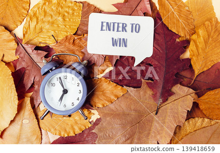 Alarm clock on autumn leaves with a speech bubble inviting to enter a contest or giveaway Alarm clock on autumn leaves with a speech bubble inviting to enter a contest or giveaway 139418659