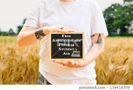 Individual holding chalkboard sign promoting federal student aid in a golden field setting Individual holding chalkboard sign promoting federal student aid in a golden field setting 139418709