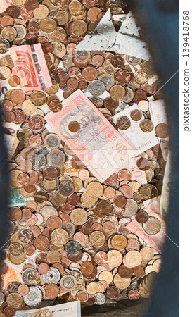 Pile of assorted coins and banknotes in a container showcasing currency diversity and value Pile of assorted coins and banknotes in a container showcasing currency diversity and value 139418768