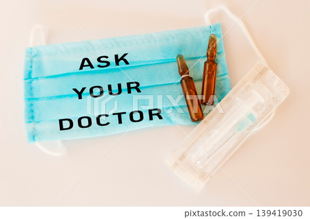 Medical mask with text, vials, and syringe on a clean surface for healthcare awareness Medical mask with text, vials, and syringe on a clean surface for healthcare awareness 139419030