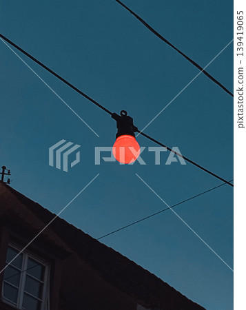 Red light bulb hanging from wire against a twilight sky illuminating urban atmosphere Red light bulb hanging from wire against a twilight sky illuminating urban atmosphere 139419065