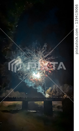 Colorful fireworks burst in the night sky above a bridge, creating a vibrant display of light and smoke, celebrating a festive occasion with excitement and joy Colorful fireworks burst in the night sky above a bridge, creating a vibrant display of light and smoke, celebrating a festive occasion with excitement and joy 139419066