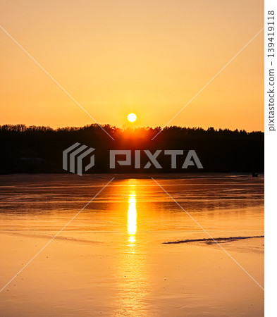 Sunset over tranquil lake reflecting golden hues with silhouettes of trees in the background Sunset over tranquil lake reflecting golden hues with silhouettes of trees in the background 139419118