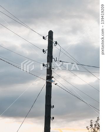 Wooden utility pole stands tall against a dramatic sky filled with clouds, showcasing electrical wires and the essence of urban infrastructure 139419209