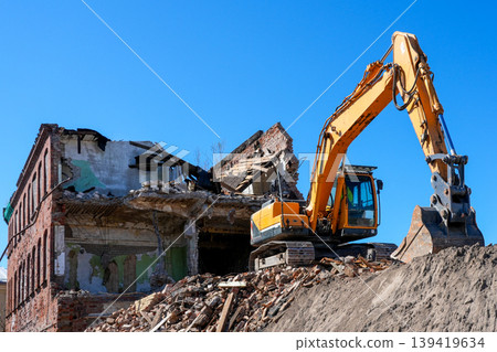 Excavator demolishing old brick building amid rubble on urban construction demolition site scene Excavator demolishing old brick building amid rubble on urban construction demolition site scene 139419634