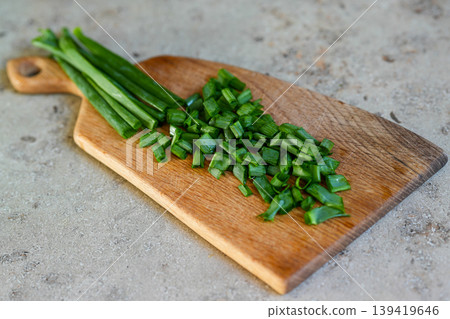 Chopped green onions on wooden cutting board in rustic kitchen food preparation closeup scene Chopped green onions on wooden cutting board in rustic kitchen food preparation closeup scene 139419646