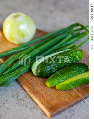 Closeup of fresh cucumbers and green onions on wooden board in rustic kitchen natural light scene 139419647