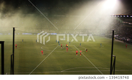 Wide view of football match with players on field in stadium, competitive sports scene, team play, outdoor game, match action. Wide view of football match with players on field in stadium, competitive sports scene, team play, outdoor game, match action. 139419748