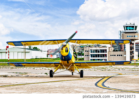 A yellow single-engine ultralight aircraft on the airfield runway. 139419873