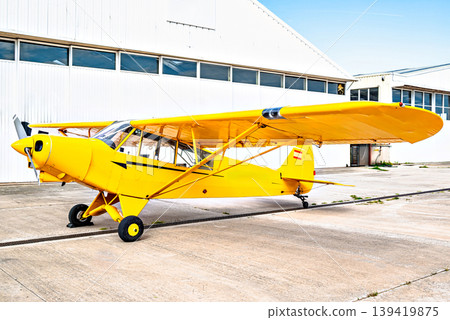 A yellow single-engine ultralight aircraft on the airfield runway. 139419875