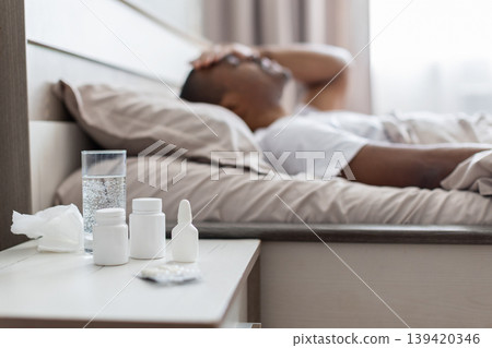 African american man lying sick in bed with medicines on bedside table African american man lying sick in bed with medicines on bedside table 139420346