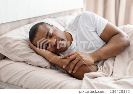 African american man sleeping peacefully in bed with relaxed expression in bedroom African american man sleeping peacefully in bed with relaxed expression in bedroom 139420353