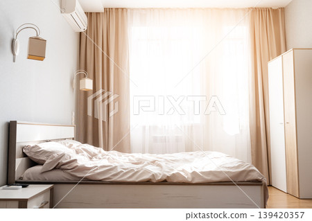 Bright, cozy bedroom interior with unmade bed, beige curtains and air conditioner Bright, cozy bedroom interior with unmade bed, beige curtains and air conditioner 139420357