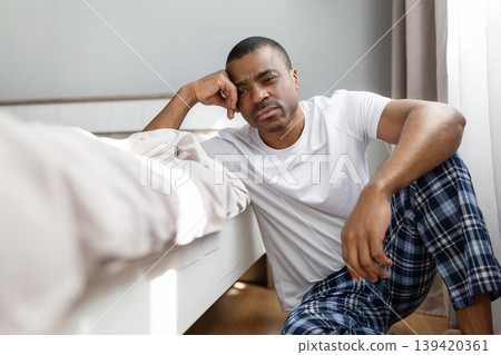 African american man sitting on floor beside bed, leaning with tired expression 139420361