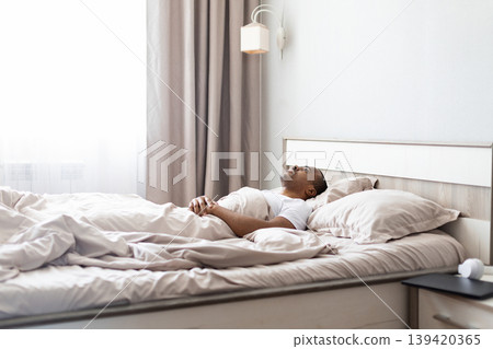 African american man lying on bed looking upward in bedroom African american man lying on bed looking upward in bedroom 139420365