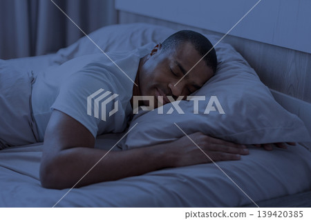 African american man sleeping at night in bedroom with blue light tone African american man sleeping at night in bedroom with blue light tone 139420385