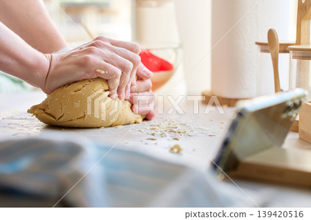 Hands kneading dough on floured kitchen surface near smartphone Hands kneading dough on floured kitchen surface near smartphone 139420516