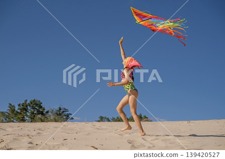 A child launches a rainbow kite into the sky, running after it. A child on a beach vacation A child launches a rainbow kite into the sky, running after it. A child on a beach vacation 139420527
