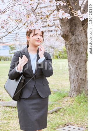 A young female businesswoman in a recruitment suit, a new employee, talks on her smartphone under a cherry tree. 139420559