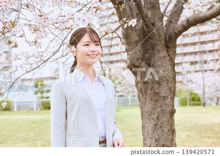 A young female new employee smiling under a cherry blossom tree - a spring freshers image - a businesswoman in a suit. 139420571