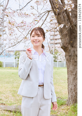 A young woman in a white suit smiles under a cherry tree - a spring portrait, an image of a new beginning. 139420574