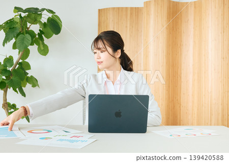 一位年輕的職業婦女在辦公室裡用筆記型電腦查看文件,分析圖表。 一位年輕的職業婦女在辦公室裡用筆記型電腦查看文件,分析圖表。 139420588