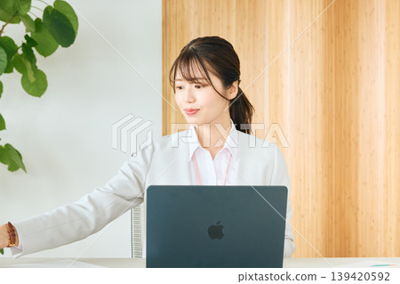 A young female business person reviewing documents on her laptop in the office; a company employee in a white suit. A young female business person reviewing documents on her laptop in the office; a company employee in a white suit. 139420592