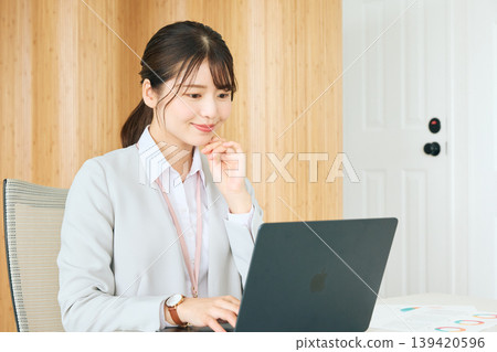 A young female business person operating a laptop in the office; a company employee in a suit working on his PC with a smile. 139420596