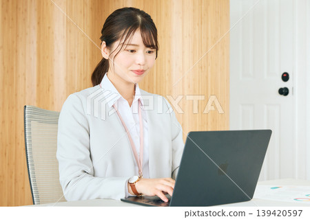 A young female business person operating a laptop in the office; a company employee in a suit concentrating on his work. 139420597