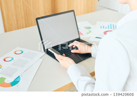 A female business professional checking data documents using her smartphone and laptop in the office. 139420608