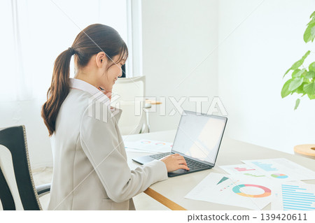 A young businesswoman and a company employee in a suit are seen in the office, with the employee checking documents on a laptop. 139420611