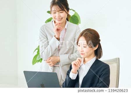 Two young Japanese female business professionals are having a meeting in their office, looking at their laptop screens. Two young Japanese female business professionals are having a meeting in their office, looking at their laptop screens. 139420623