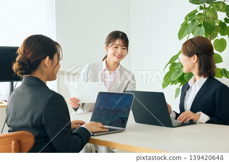 三位女性商務人士正在辦公室會議室開會，她們手持文件，討論團隊合作和談判。 139420648