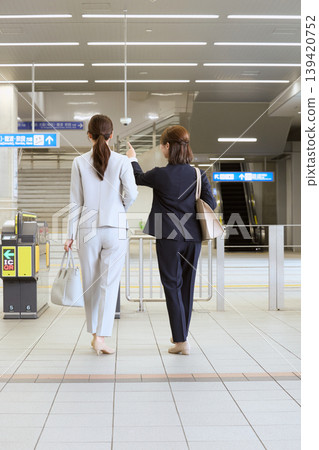 Two female business people walking near the station ticket gates; the backs of office workers in suits commuting to work. Two female business people walking near the station ticket gates; the backs of office workers in suits commuting to work. 139420752