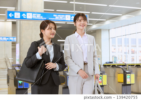 兩名身穿職業套裝的年輕女子，正穿過火車站的檢票口——通勤場景——一位商務女性出差的畫面。 139420755