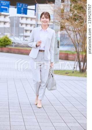 A young businesswoman in a white suit walks through the city streets in springtime; a Japanese female office worker smiles as she commutes to work. A young businesswoman in a white suit walks through the city streets in springtime; a Japanese female office worker smiles as she commutes to work. 139420767