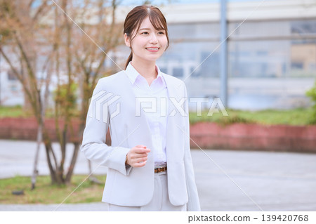 A young female businessperson in a white suit smiling outdoors – an image of a new employee in spring. 139420768