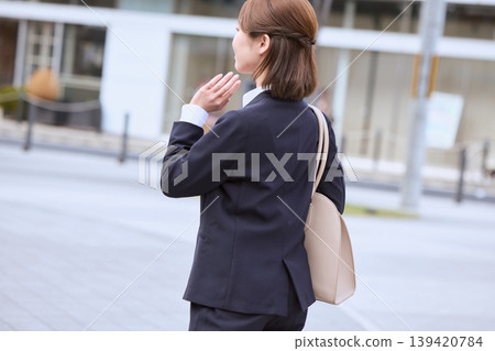 A young businesswoman in a suit waving as she walks through the office district; behind her, a woman in a recruitment suit who is looking for a job. A young businesswoman in a suit waving as she walks through the office district; behind her, a woman in a recruitment suit who is looking for a job. 139420784