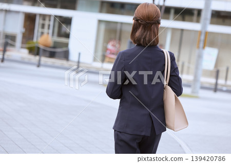 一位身著職業套裝的女商人走在辦公街上,鏡頭從背後拍攝。 一位身著職業套裝的女商人走在辦公街上,鏡頭從背後拍攝。 139420786