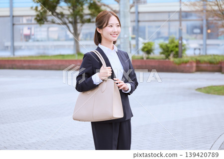 A young Japanese businesswoman in a suit, carrying a beige bag, walking outdoors – an image of a job seeker or commuter. A young Japanese businesswoman in a suit, carrying a beige bag, walking outdoors – an image of a job seeker or commuter. 139420789