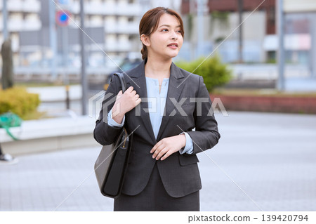 A young businesswoman walking outside with a business bag; a company employee in a suit heading out for a sales call. A young businesswoman walking outside with a business bag; a company employee in a suit heading out for a sales call. 139420794