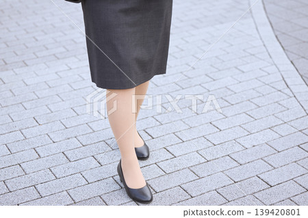 A woman's feet in a business suit skirt and pumps walking – an image of job hunting or commuting to the office. A woman's feet in a business suit skirt and pumps walking – an image of job hunting or commuting to the office. 139420801