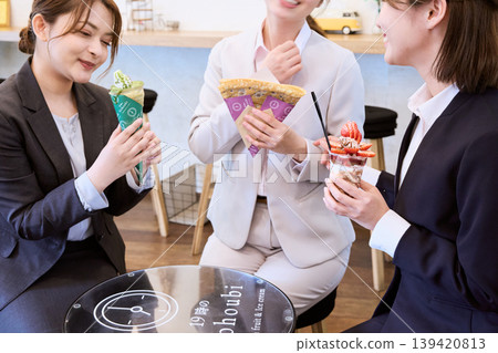 三位身著職業套裝的女士下班後在咖啡館享用可麗餅和芭菲——這是她們應得的甜蜜犒勞。 三位身著職業套裝的女士下班後在咖啡館享用可麗餅和芭菲——這是她們應得的甜蜜犒勞。 139420813